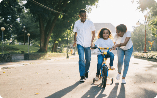 A family on the street helping their daughter ride her bike