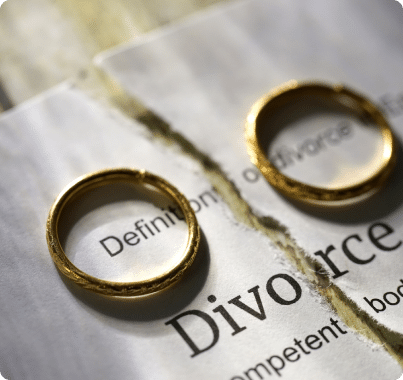 Two wedding rings on top of a ripped divorce document